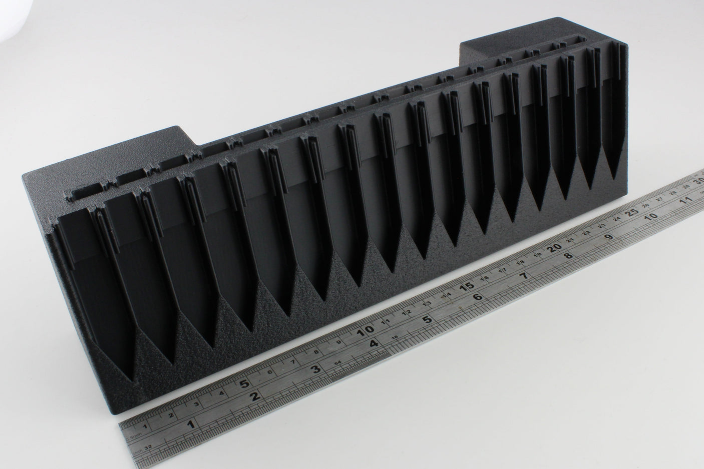 Black plastic component with a ruler for scale on a white background