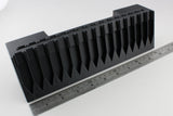Black plastic component with a ruler for scale on a white background