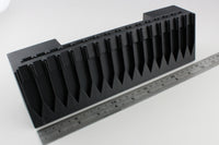 Black plastic component with a ruler for scale on a white background