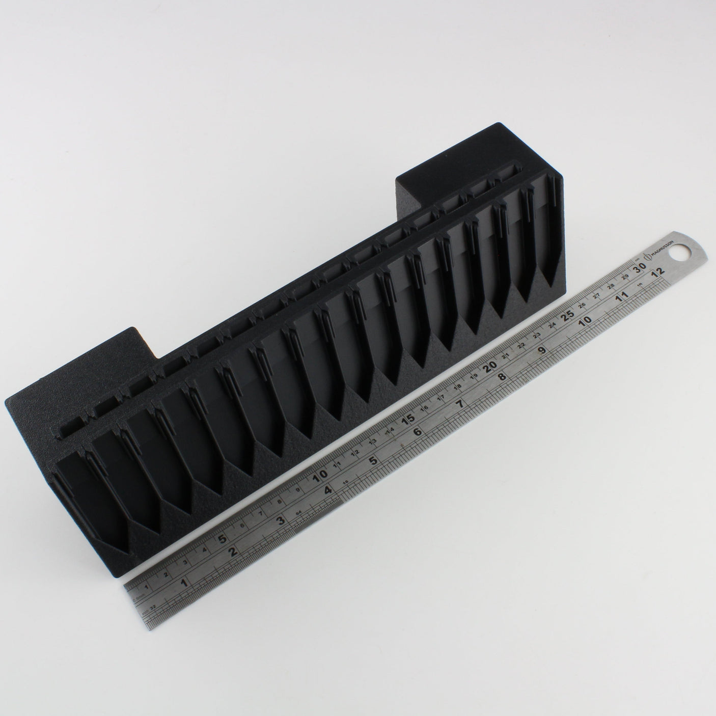 Black plastic component with a ruler for scale on a white background
