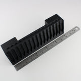 Black plastic component with a ruler for scale on a white background