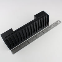 Black plastic component with a ruler for scale on a white background