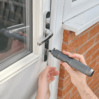 Person using a Dangerfield Machina Electric Lock Pick Gun on a door handle with a brick wall background